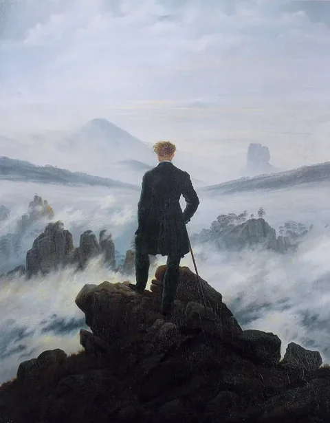 A man in dark clothing stands on a rocky precipice with his back to us, gazing out over a sea of fog and distant mountain peaks