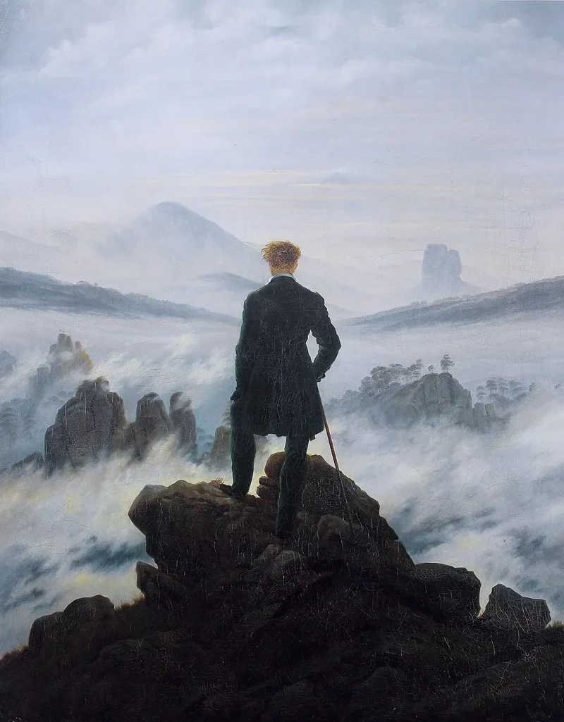 A man in dark clothing stands on a rocky precipice with his back to us, gazing out over a sea of fog and distant mountain peaks